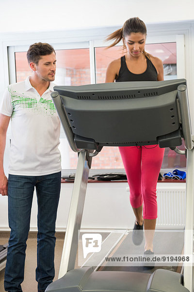 Instruktorin  die eine Frau auf einem Laufband in einem Fitnessstudio unterrichtet.