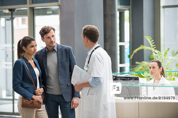 Male doctor discussing with couple at hospital reception desk