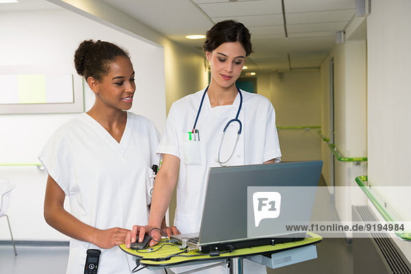 Female doctor and nurse using laptop in hospital corridor