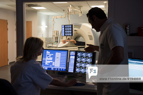 Doctors examining scan on computer with patient on MRI scanner in background