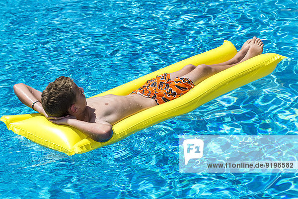 Boy 12 years lying on a lilo in a swimming pool