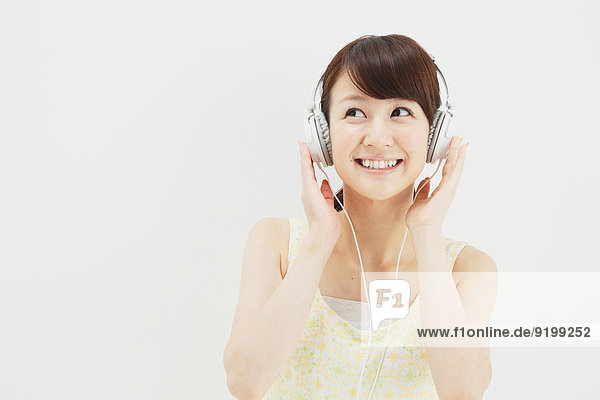 Japanese young woman in a one piece dress with earphones standing against white background