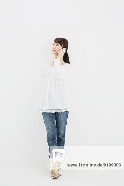 Japanese young woman in jeans and white shirt with smartphone standing against white background