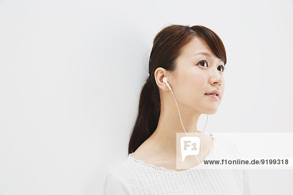 Japanese young woman in jeans and white shirt with earphones standing against white background