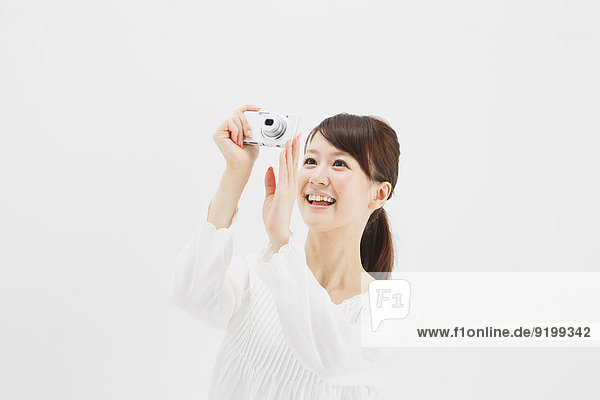 Japanese young woman in a white shirt with digital camera against white background
