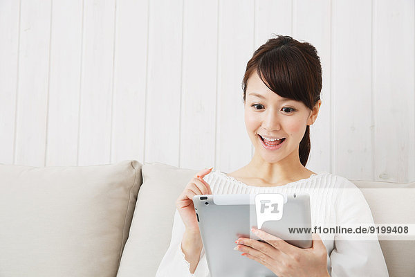 Japanese young woman in a white shirt with tablet on the sofa