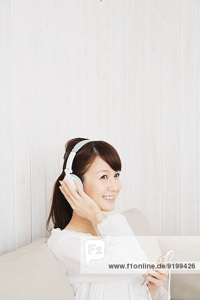 Japanese young woman in a white shirt with earphones on the sofa