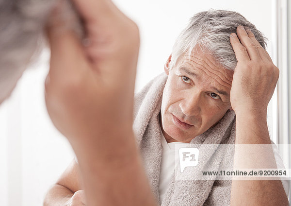 Mann vor Spiegel betrachtet seinen Haaransatz