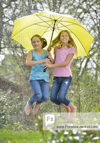 Zwei Mädchen hüpfen unter Regenschirm