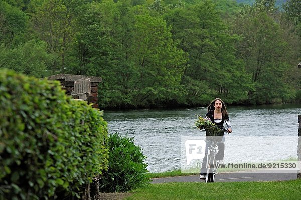 young woman cycling on cycle lane along the Meuse River at Haybes,  Ardennes department,  Champagne-Ardenne region of northeasthern France,  Europe.