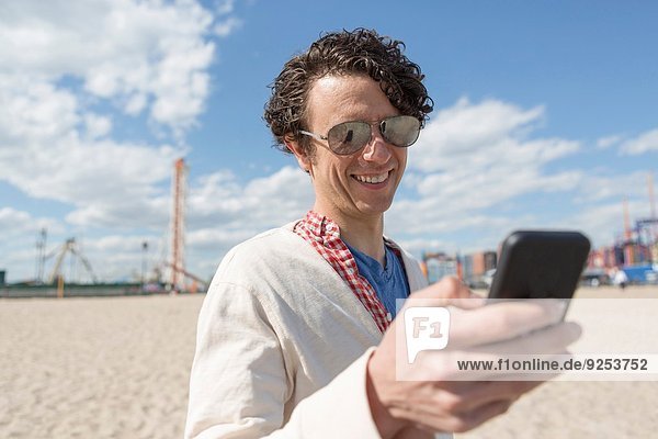 Mid Erwachsene Mann SMS auf Smartphone am Strand