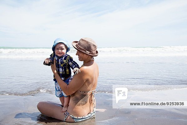 Young woman sitting in sea with baby son