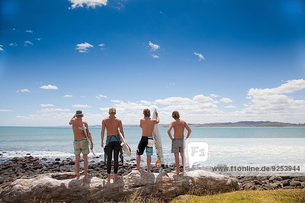 Four young male surfer friends watching sea from rocks