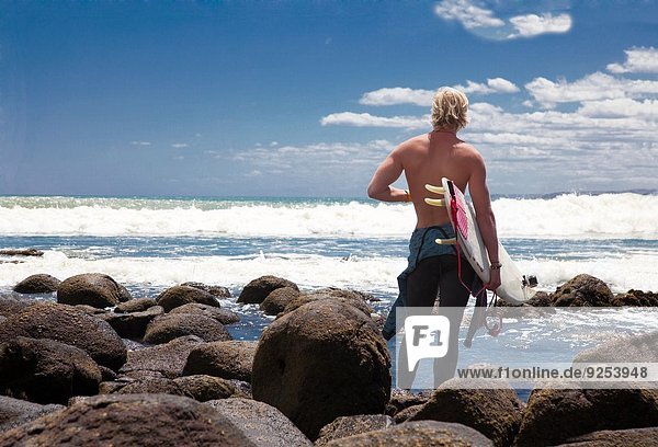Junge erwachsene männliche Surfer beobachten das Meer von den Strandfelsen aus.