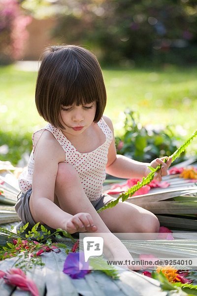 Girl with fern making flower and leaf display in garden