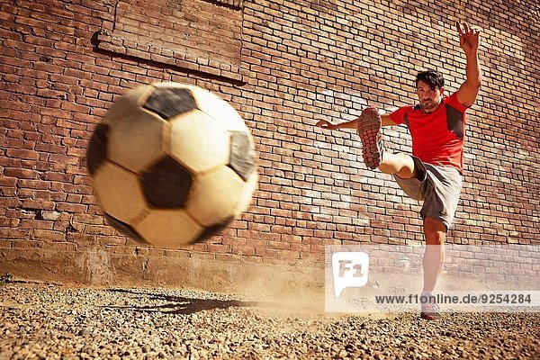 Junger Mann tritt Fußball auf Ödland