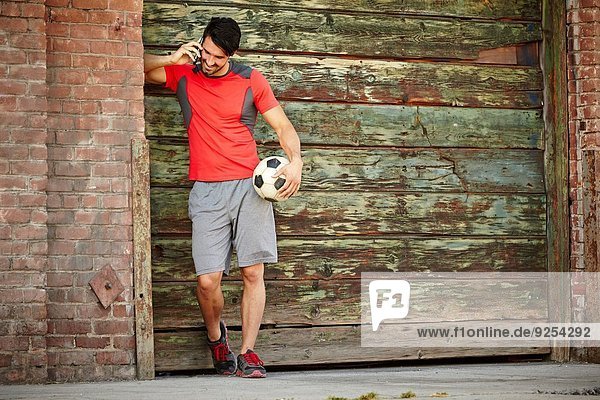 Young male soccer player chatting on smartphone