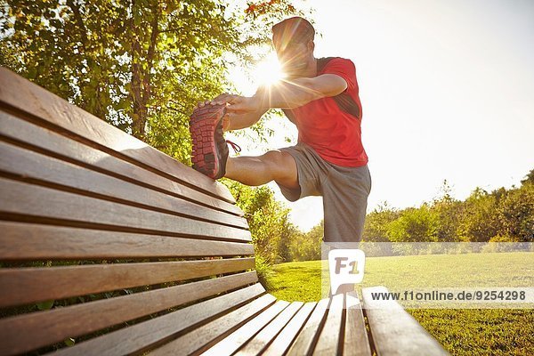 Young male runner stretching legs on park bench