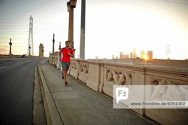Young man running across city bridge at sunrise