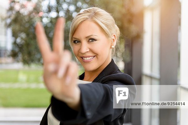 Portrait of young businesswoman making victory sign