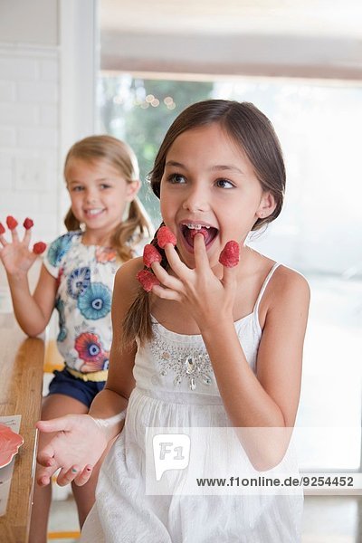 Zwei Schwestern mit Himbeeren an den Fingern in der Küche