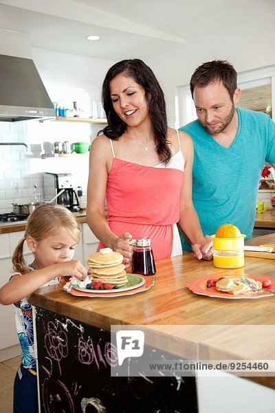 Mittlere erwachsene Eltern beobachten die Tochter  die von Pfannkuchen an der Frühstücksbar versucht wird.