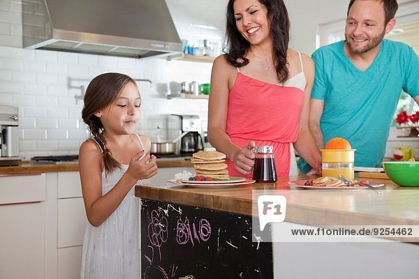 Mittlere erwachsene Eltern verführerische Tochter mit Pfannkuchen an der Frühstückstheke
