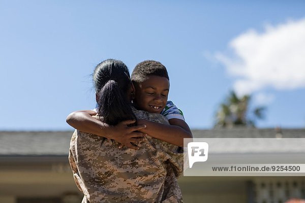 Rückansicht einer Soldatin  die ihren Sohn beim Homecoming umarmt.