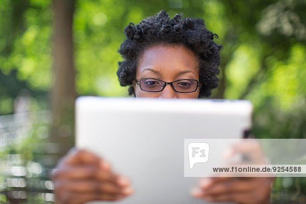 Junge Frau im Park hält hoch und liest digitales Tablett