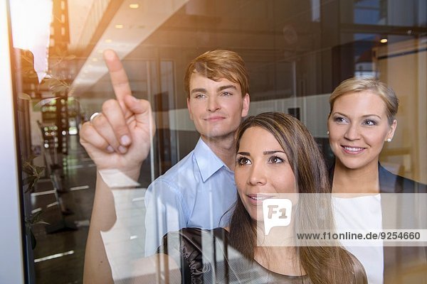 Businesswoman pointing out of glass window to colleagues
