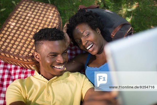 Junges Paar im Park liegend mit einem Selfie auf digitalem Tablett