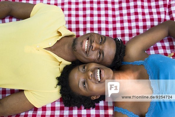 Overhead-Porträt eines jungen Paares  das auf einer Picknickdecke auf gegenüberliegenden Seiten liegt