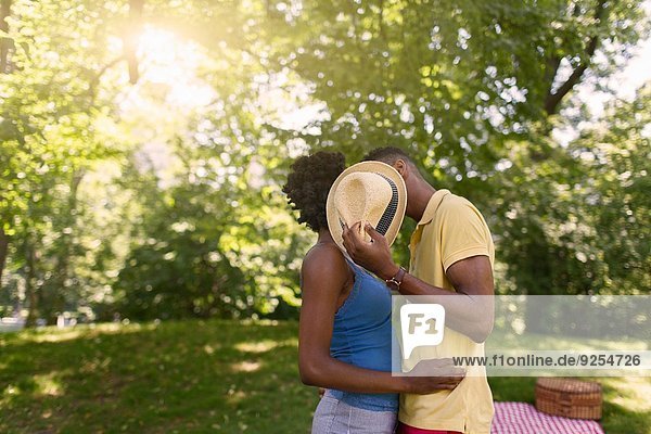 Junges Paar im Park hält den Hut hoch  um Gesichter zu verdecken.