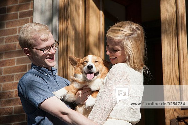 Happy young couple with corgi dog in arms outside front door