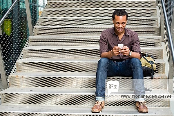 Young man texting on smartphone on city stairway