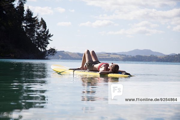 Mittlere erwachsene Frau beim Sonnenbaden auf dem Paddelbrett auf See