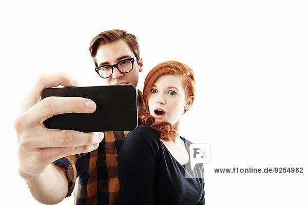 Studioaufnahme eines jungen Paares  das für Selfie auf dem Smartphone posiert.