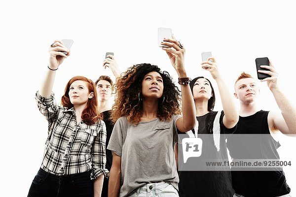 Studio-Porträt von fünf jungen Erwachsenen auf Smartphones
