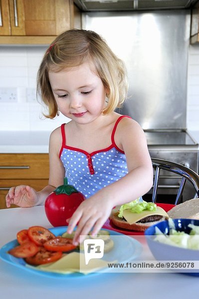 Kleines Mädchen belegt Hamburger mit Tomaten