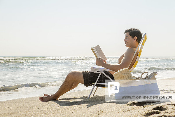 Side view of man sitting on deckchair and reading book