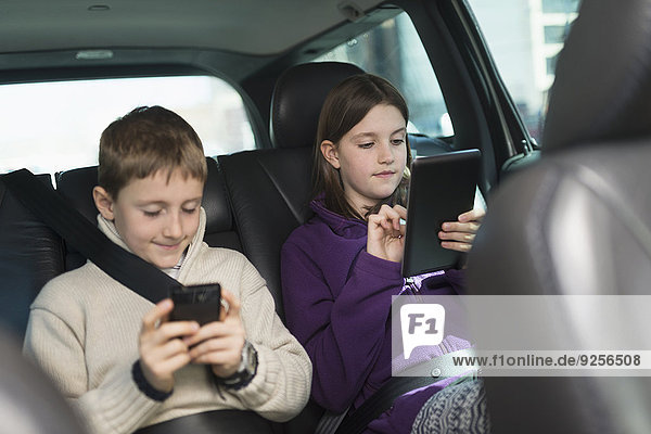 Boy and girl (8-9  10-11) using digital tablet and smart phone in car