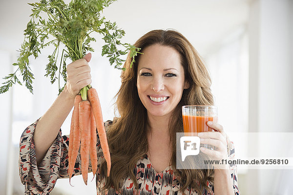 Portrait of woman holding carrots and carrot juice