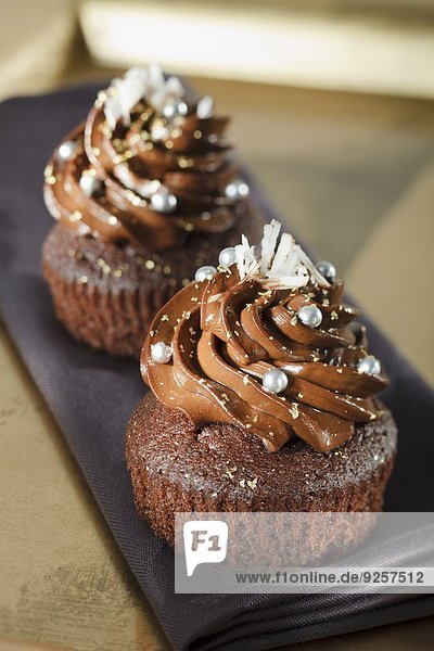 Schokoladen-Cupcakes mit silbernen Zuckerperlen und weissen Schokoraspeln