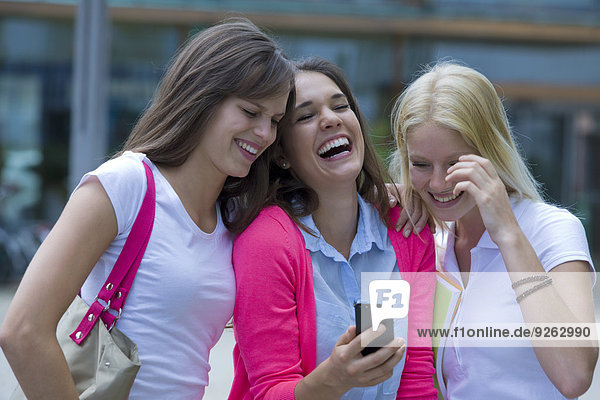 Deutschland  Baden-Württemberg  Porträt von drei lachenden jungen Studentinnen mit Smartphone