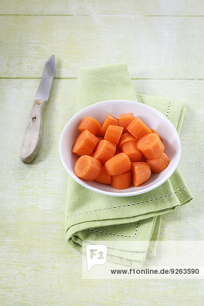 Schale mit geschnittenen Karotten  Küchenmesser und Tuch auf Holz