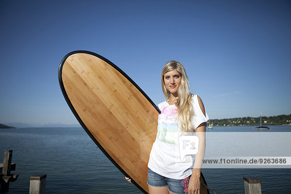 Porträt einer jungen Frau mit Surfbrett vor einem See