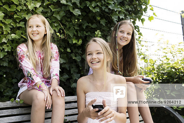 Drei lächelnde Mädchen sitzen auf einer Parkbank.