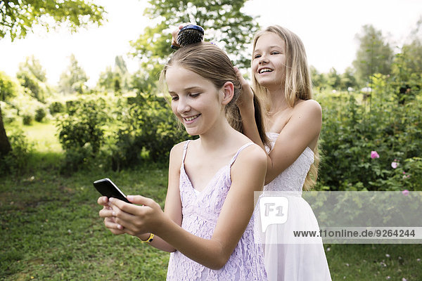 Girl using her smartphone while her sister brushing her hair