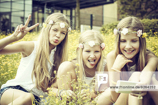 Porträt von drei Mädchen mit Blumenkränzen  die einen Selfie auf einer Blumenwiese tragen.