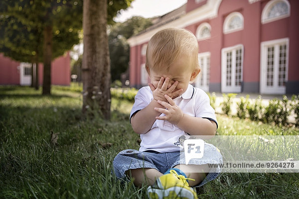 Germany  Oberhausen  Blond baby boy sitting in park of Oberhausen Castle
